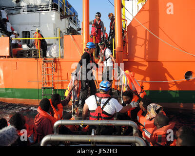 Corigliano Calabro, Italien. 29. Juni 2017.  Migranten (vorne) warten einem Brett ein kleines Boot, eine so genannte RHIB, deren Übertragung auf das Rettungsschiff "Aquarius" im Mittelmeer, 27. Juni 2017. Die Hilfsorganisationen Ärzte ohne Grenzen und SOS Méditerranée brachte sie nach Italien, nach dem Speichern sie aus Seenot. Foto: Lena Klimkeit/Dpa/Alamy Live-Nachrichten Stockfoto