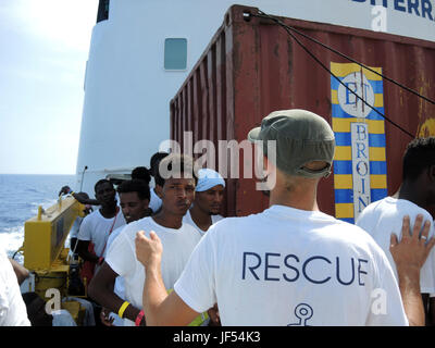 Ein Helfer auf dem Rettungsschiff "Wassermann" leitet die Migranten, die neu auf dem Boot im Mittelmeer, 28. Juni 2017 angekommen sind. Die humanitäre Hilfe Rettung Organisation Ärzte ohne Grenzen und SOS Méditerranée Flüchtlinge, die in die Europäische Union auf allen anderen Strecken, die Einreise verweigert werden nach Italien zu bringen. Foto: Lena Klimkeit/dpa Stockfoto