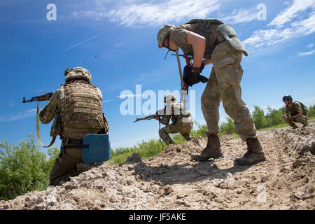 Ein Soldat der ukrainischen Armee aus dem 1. Airmobile Bataillon, 79. Air Assualt Brigade zeigt die Richtung an zwei seiner Soldaten während einer live-Brandabschnitt Angriff Übung im Yavoriv Combat Training Center, im Westen der Ukraine, während ein Beobachter Controller Trainer von der CTC beobachtet.    Yavoriv CTC-Personal zusammen mit Mentoren aus der US-Armee 45. Infantry Brigade Combat Team, führte die Ausbildung zum Soldaten von der 1-79. während der Rotation des Bataillons durch Yavoriv CTC. 45. ist die Ukraine als Teil der gemeinsamen multinationalen Training Gruppe-Ukraine, ein international bereitgestellt. Stockfoto