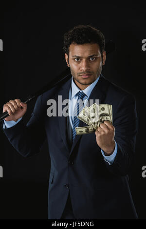 Ernst junger Geschäftsmann Baseball-Schläger und Dollar-Banknoten Blick in die Kamera halten Stockfoto