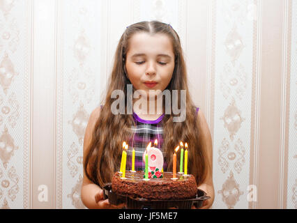 kleines Mädchen bläst Kerzen auf der Torte am Tag ihrer Geburt 9 Jahre Stockfoto