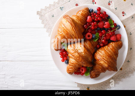 Frisch gebackene Croissants mit Himbeeren, Heidelbeeren und Johannisbeeren Nahaufnahme auf einer Platte. horizontale Ansicht von oben Stockfoto