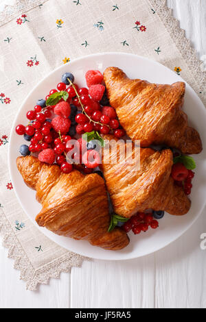 Leckeres Buttercroissant mit frischen Beeren hautnah auf einem Teller. Vertikale Ansicht von oben Stockfoto