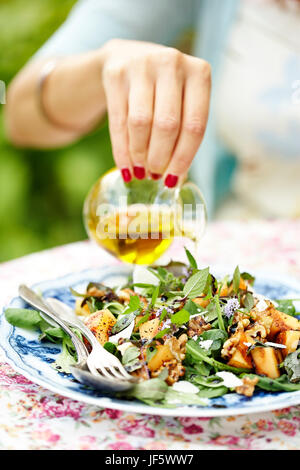 Womans hand hinzufügen von Öl in den Salat Stockfoto
