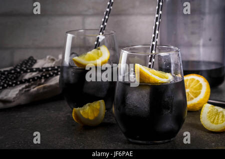 Trendige Lebensmittel. Sommer-Erfrischung Getränke. Entgiftung und Ernährung Konzept. Schwarz mit Holzkohle, Eis, Zitronensaft und Zitronen-Limonade. Auf einem Hause Steintisch mit Stockfoto