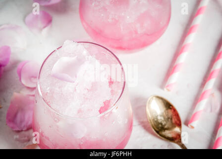 Sommer erfrischende Desserts. Vegane Ernährung essen. Eis, gefrorene rose, erstarrte und mit Rosenblättern und Roséwein. Auf einem weißen Betontisch mit Löffeln, str Stockfoto