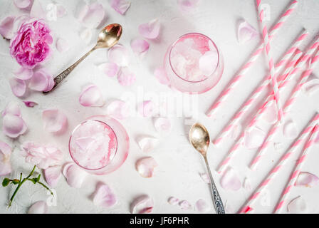 Sommer erfrischende Desserts. Vegane Ernährung essen. Eis, gefrorene rose, erstarrte und mit Rosenblättern und Roséwein. Weiße Betontisch mit Löffeln, gestreift Stockfoto