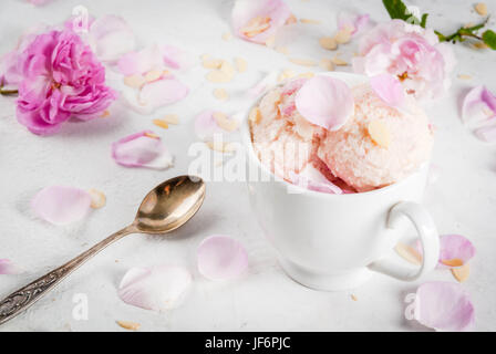 Sommer erfrischende Desserts. Vegane Ernährung essen. Eis mit Rosenblättern und Scheiben von Mandeln, weißen Schüsseln auf einem weißen Beton Tisch. Kopie Stockfoto