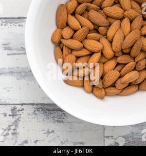 Mandeln in einer weißen Schüssel auf einem rustikalen Tisch in ein quadratisches Format Stockfoto