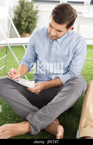 Barfuß Jungunternehmer sitzen und schreiben auf Papier mit Bleistift Stockfoto