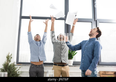 Fröhliche junge Geschäftsleute triumphiert und Papiere in Büro, Teamarbeit Geschäftskonzept zu werfen Stockfoto