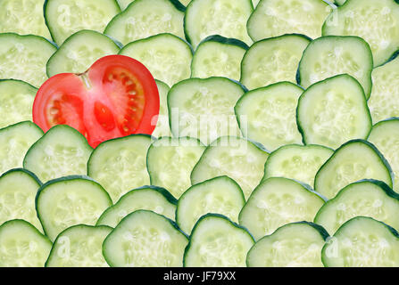 Eine Scheibe rote Tomate zwischen vielen geschnittenen Gurken. Guter Hintergrund Stockfoto