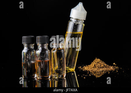 E-Liquid-Flaschen neben gemahlenen Tabakblättern und Rauchwolke Stockfoto