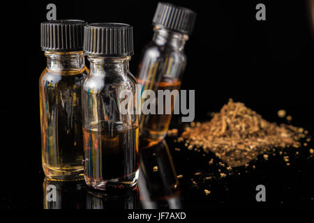 E-Liquid-Flaschen neben gemahlenen Tabakblättern Stockfoto