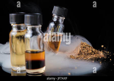 E-Liquid-Flaschen neben gemahlenen Tabakblättern und Rauchwolke Stockfoto