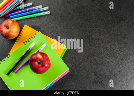 Zurück zur Schule. Obst (Äpfel) mit Notebooks, farbige Stifte auf einem schwarzen Tisch. Kopieren Sie Raum Draufsicht Stockfoto