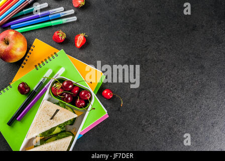 Zurück zur Schule. Ein herzhaftes gesundes Schulessen in einer Box: Sandwiches mit Gemüse und Käse, Beeren und Früchte (Äpfel) mit Notebooks, farbigen Stift Stockfoto