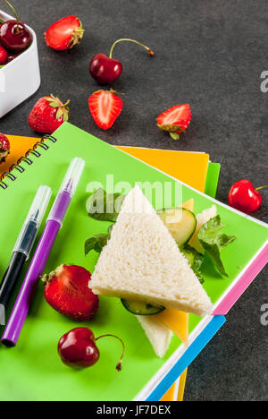 Zurück zur Schule. Ein herzhaftes gesundes Schulessen in einer Box: Sandwiches mit Gemüse und Käse, Beeren und Früchte (Äpfel) mit Notebooks, farbigen Stift Stockfoto