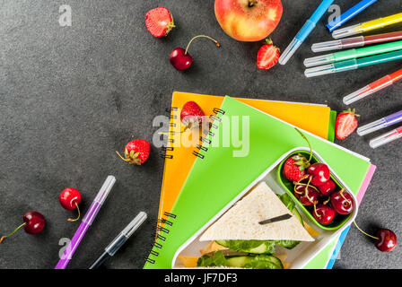 Zurück zur Schule. Ein herzhaftes gesundes Schulessen in einer Box: Sandwiches mit Gemüse und Käse, Beeren und Früchte (Äpfel) mit Notebooks, farbigen Stift Stockfoto