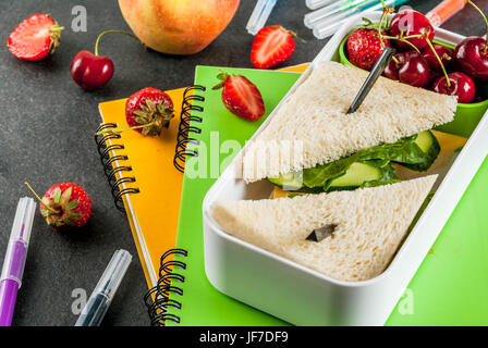 Zurück zur Schule. Ein herzhaftes gesundes Schulessen in einer Box: Sandwiches mit Gemüse und Käse, Beeren und Früchte (Äpfel) mit Notebooks, farbigen Stift Stockfoto