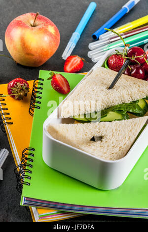 Zurück zur Schule. Ein herzhaftes gesundes Schulessen in einer Box: Sandwiches mit Gemüse und Käse, Beeren und Früchte (Äpfel) mit Notebooks, farbigen Stift Stockfoto