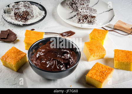 Australische Küche. Vorbereitung der traditionellen australischen Dessert Lamington: Biskuit in Schokolade mit Kokos Rasur Pulver. Weißen Tisch.  Kopieren von spac Stockfoto