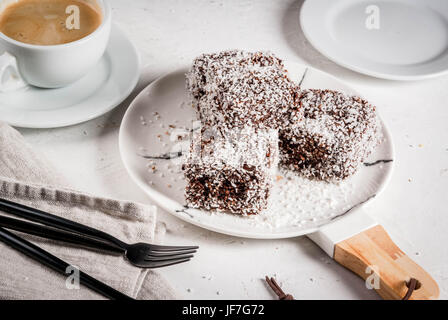 Australische Spezialitäten. Traditionelles Dessert Lamington - Stücke Zwieback in dunkler Schokolade bestreut mit Kokos Pulver Chips zu rasieren. Auf einer Marmorplatte Stockfoto