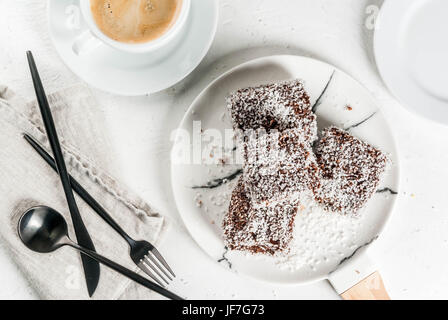 Australische Spezialitäten. Traditionelles Dessert Lamington - Stücke Zwieback in dunkler Schokolade mit Kokos Pulver Chips bestreut. Auf einer Marmorplatte weiß ta Stockfoto