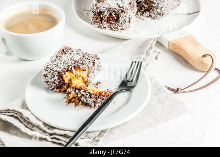 Australische Spezialitäten. Traditionelles Dessert Lamington - Stücke Zwieback in dunkler Schokolade mit Kokos Pulver Chips bestreut. Auf einer Marmorplatte weiß ta Stockfoto