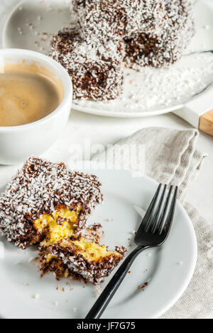 Australische Spezialitäten. Traditionelles Dessert Lamington - Stücke Zwieback in dunkler Schokolade mit Kokos Pulver Chips bestreut. Auf einer Marmorplatte weiß ta Stockfoto