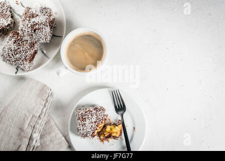 Australische Spezialitäten. Traditionelles Dessert Lamington - Stücke Zwieback in dunkler Schokolade mit Kokos Pulver Chips bestreut. Auf einer Marmorplatte weiß ta Stockfoto