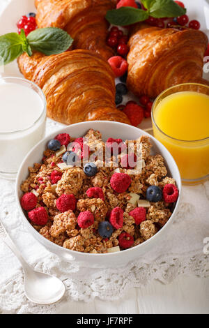 Müsli mit getrockneten Beeren und weißer Schokolade, Croissants, Milch und Orangensaft Nahaufnahme auf dem Tisch. vertikale Stockfoto