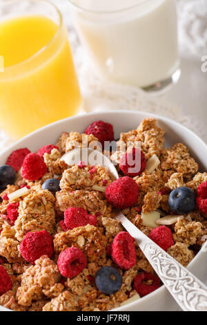 Leckeres Frühstück mit Müsli mit getrockneten Himbeeren, Nüssen und Heidelbeeren, Milch und Saft Makro auf dem Tisch. vertikale Stockfoto