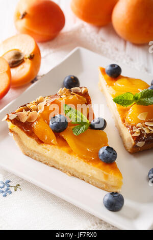 Käsekuchen mit Aprikosen, Blaubeeren, Minze und Mandeln Nahaufnahme auf einem Teller auf den Tisch. vertikale Stockfoto