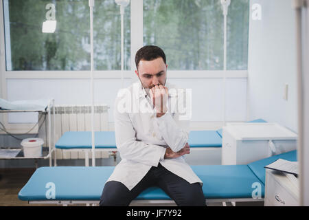 Nachdenklich Arzt sitzen in einem OP-Saal mit seiner Hand auf Kopf Stockfoto