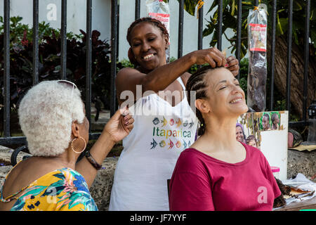 Ein Tourist bekommt ihr Haar geflochten in der PLAZA DE ARMAS in HABANA VIEJA - Havanna Kuba Stockfoto