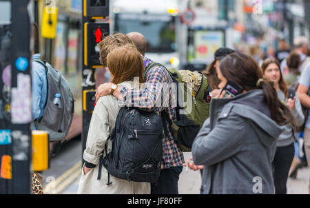 Alltägliche Szene, in der ein junges Paar mit Armen umeinander in einer Stadt voller Menschen in England, Großbritannien, dargestellt wird. Stockfoto