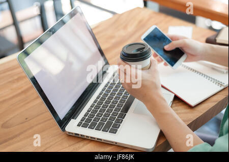 Asiatische Hipster mit männlichen Smartphone für soziales Netzwerk und Kaffee trinken während der Arbeit mit dem Laptop im Coffee Shop. Freiberufler Lebensstil und Stockfoto