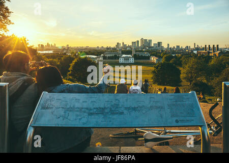 Menschen sitzen auf einem Hügel im Greenwich Park, London, beobachten den Sonnenuntergang und die Fotos. Jedes Jahr werden Millionen von Londoner und Touristen Stockfoto