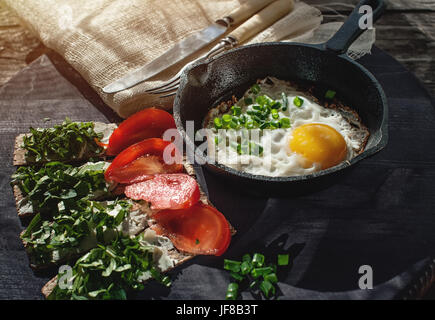 Rührei und Brötchen mit Käse, Grüns und Tomaten im rustikalen Stil. Kunst. Stockfoto