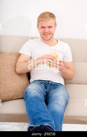 Junger Mann, ein Sandwich zu essen zu Hause Stockfoto