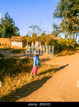 Malawische Kind steht am Rand der Schotterstraße durch ländliche Dorf zeigt traditionell gebaut Schlamm Gehäuse Stockfoto