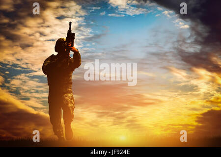 Soldat im Kampfschiessen mit seiner Waffe, Gewehr bei Sonnenuntergang. Krieg, Armee, Militär. Stockfoto