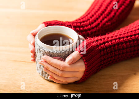 Heiße Tasse Tee Erwärmung Frauenhand in Retro-wollene Pullover. Tisch aus Holz Stockfoto