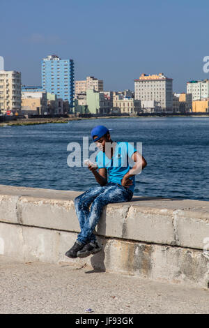 Junger kubanischen Mann nutzt sein Handy sitzt auf dem MALECON - Havanna, Kuba Stockfoto