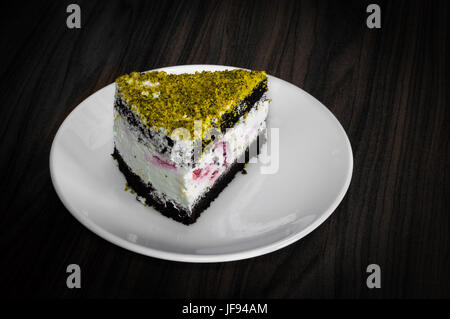 Berry und Schokoladenkuchen mit Pistazien garniert serviert in einem weißen Teller auf einem Holztisch Stockfoto