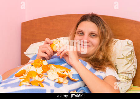 Fröhliches Mädchen isst Mandarinen im Bett liegend Stockfoto