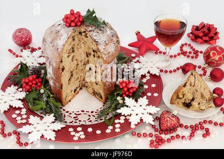 Italienische Schokolade Panettone Weihnachtskuchen und Scheibe mit Glas Sherry, Schneeflocke und Rote Christbaumkugel-Dekorationen, Stechpalme, Mistel, Tanne und Kiefer Kegel Stockfoto