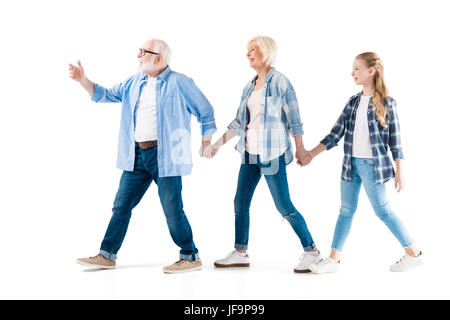 glückliche Großvater, Großmutter und Enkelin zu Fuß und Hand in Hand zusammen isoliert auf weiss Stockfoto