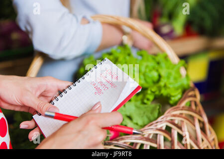 Junge Frau überprüfen kauft Liste. Mädchen mit einem Notebook in Händen. Einkaufsliste in der hand. Stockfoto